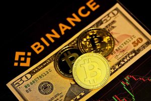 A photo of the Binance logo with a fifty dollar bill and a Bitcoin.